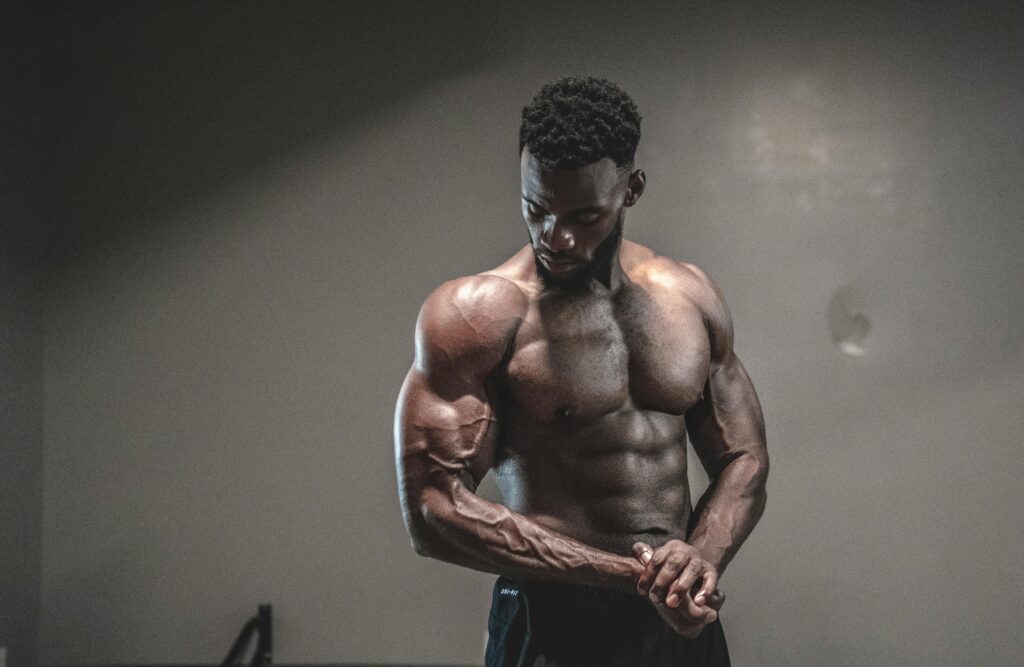 A strong, shirtless male bodybuilder showcasing muscles and strength in a gym setting. ManUp Gummies
