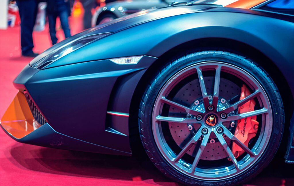 Detailed view of a luxury sports car wheel on a red carpet at an auto show. acessórios automotivos